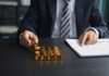El precio del oro sigue subiendo, con un 11 por ciento de ganancia respecto al mínimo de este año Businessperson in a dark suit places gold bars on a desk beside a document.