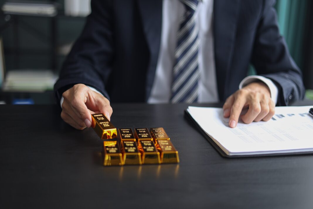 Businessperson in a dark suit places gold bars on a desk beside a document.