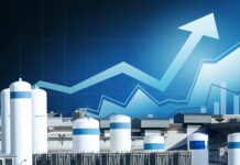 Hydrogen Fuel Cell Stocks: How to Separate the Technology Story From the Economics Industrial tanks at a facility with a blue upward-trending graph overlay in the sky